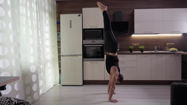 A man makes a rack on his hands at home in the background of a kitchen headset. An athlete in black uniforms trains at home during the 2020 pandemic.
