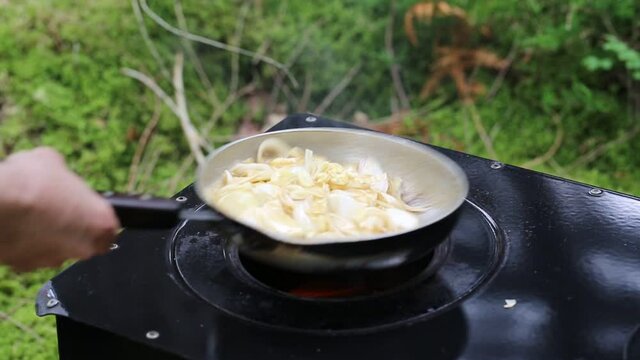 Tossing pan with caramelised onion and chopped garlic on oven outdoor