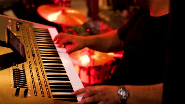 Musician playing organ keyboard following rhythm of band performing jazz music on night club