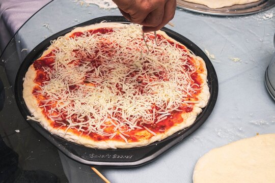 Male chef putting mozzarella cheese on top of uncooked pizza