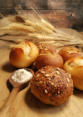 verschiedene Brötchen auf einer Holzplatte mit Getreidezweigen und Holzlöffel voll Mehl.