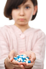 Child holds handful of pills on white background.