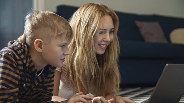 Attractive young blonde mum teaching her teenage son on laptop during self-isolation and quarantine. Female parent using online resources for studying new material. Concept of online studying.