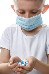 Child in medical mask holds handful of pills.