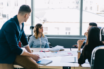 Group of creative young people discussing plan of collaboration sitting at meeting table with sketch in modern office.Team of professionals in formal wear cooperating during briefing meeting