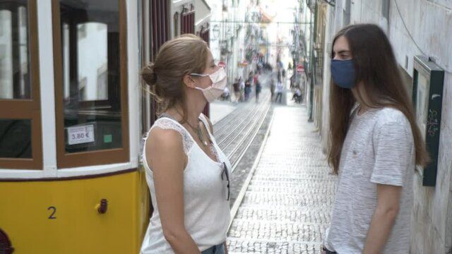 Friends With Face Mask Protection Have Conversation In Lisbon. Couple of friends talking to each other wearing a face mask on a famous street of Lisbon, Portugal. Handheld shot