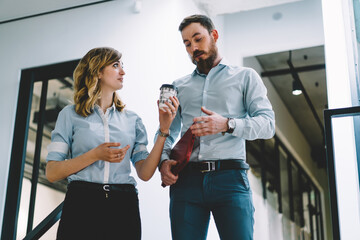 Female secretary giving tasty coffee to male buzy proud ceo dressed in formal wear.Colleague offering caffeine beverage to entrepreneur going in corridor.Friends employees having break