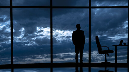 The businessman is standing near the windows in the office center