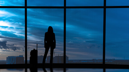 The woman with suitcase stands near the windows in the business office building