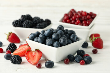 Bowls with berries on white wooden background, close up