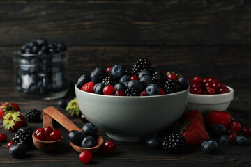 Composition with bowls of fresh berries on wooden background, space for text