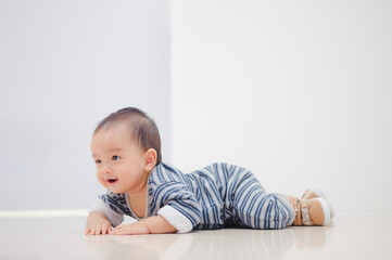 Fototapeta premium Smiling crawling asian baby boy at home on floor with white background.
