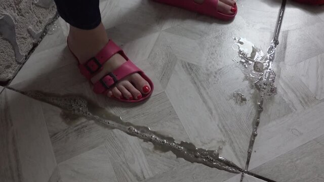 Person stepping on moving tile in the bathroom. New stone tiles damaged because of bath room flood. Hose repairs, reconstruction