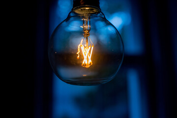 Big filament bulb with yellow light on blue background. Large LED lamps in retro style. Close up...