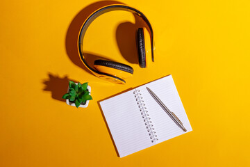 Desktop with yellow wireless headphones and an open notebook on a bright yellow background.