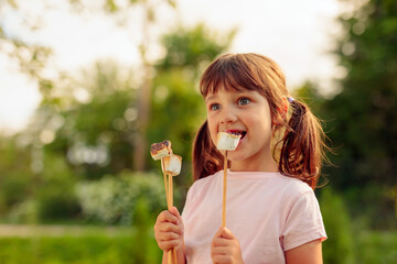Four-year-old girl eats marshmallows toasted over a fire.