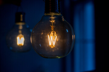 Big filament bulb with yellow light on blue background. Large LED lamps in retro style. Close up glowing light bulb. Round glowing tungsten lamp. Decorative antique tungsten light bulb. Copy space