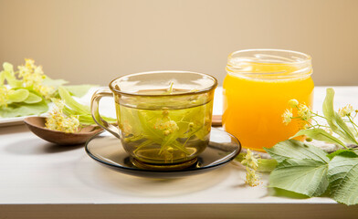 Tilia platyphyllos known as large-leaved linden herbal tea with freshly picked blossoms and jar of honey with tree leaves and branches with blossoms for decoration on wood table.