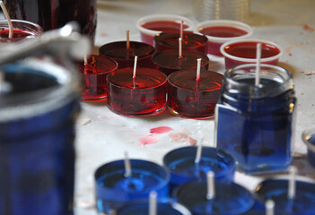 Fototapeta na wymiar Making candles in red and blue liquid wax on a chandler's bench. Tea lights and larger candles in liquid form with wicks set and candle wax drips.