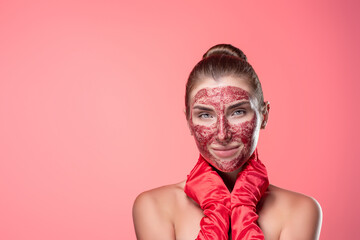 Portrait: a young woman with a red cosmetic mask on her face in red gloves posing on a pink background. Spa Cosmetic procedures. Organics