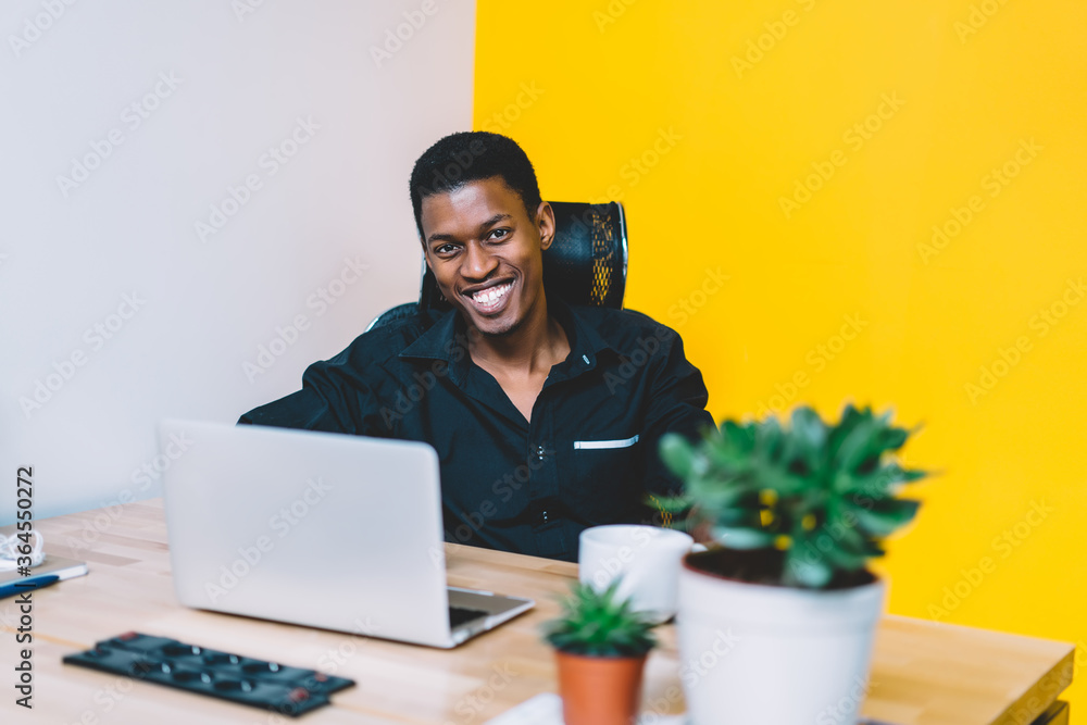 Poster portrait of cheerful african american young man dressed in formal wear laughing at camera while work