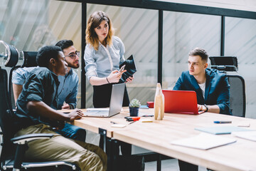 Multicultural team of male and female professionals dressed in formal wear communicating with each other and discussing collaborative plan of developing startup project during brainstorming in office