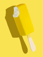 Bitten yellow ice cream bar on a stick on yellow background