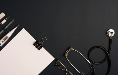 Medicine accessory, stethoscope with notepad, black background with copy space. top view