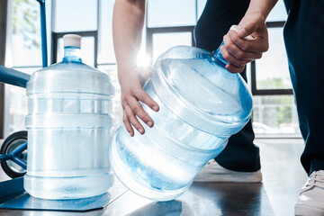 cropped view of delivery man holding blue bottle with water near hand truck