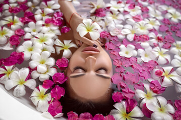 Obraz na płótnie Canvas An adorable female with closed eyes relaxes in the bath among the flower pink and white petals. Spa and relaxation. Natural makeup