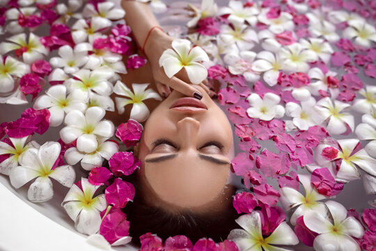 An adorable female with closed eyes relaxes in the bath among the flower pink and white petals. Spa and relaxation. Natural makeup