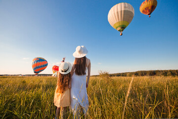 Mom and daughter pose as they launch balloons from a green field at sunset. Summer. Sunny.