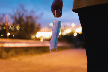Anonymous person in casual clothes standing on street in evening and holding medical mask in hand