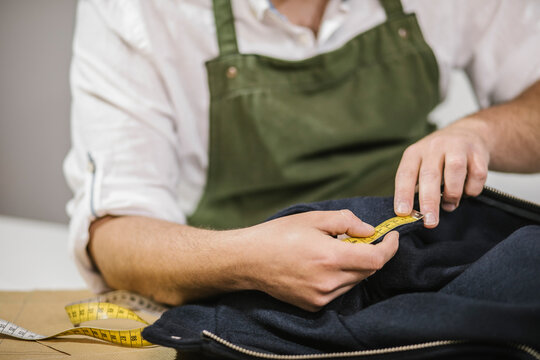 Unrecognizable male seamstress using measuring tape while checking exact size of patterns while making bespoke outfit for client in modern atelier