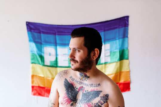 young caucasian boy with tattoos poses in front of a rainbow flag. concept of peace and lgbt.