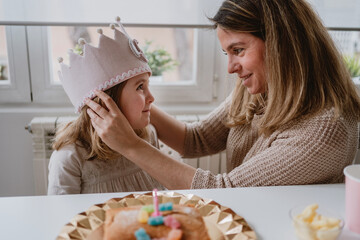 Side view of cheerful mother placing felt handmade crown on daughter while celebrating birthday together at home