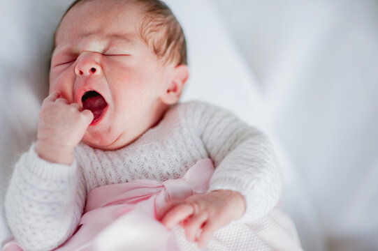 High angle of adorable baby girl in cozy dress lying in cot and yawning while sleeping