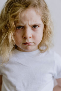 Disappointed little child in casual t shirt looking at camera on white background in studio