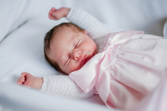 High angle of adorable baby girl in cozy dress lying in cot while sleeping