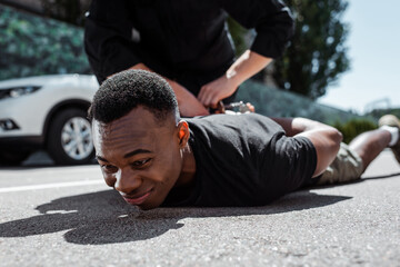 selective focus of detained african american man lying on street near policeman, racism concept