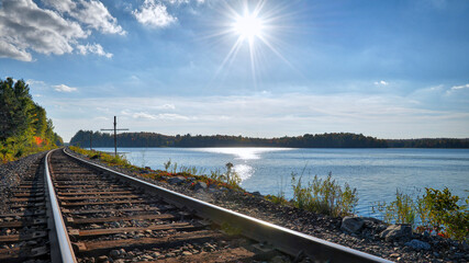 Fototapeta na wymiar Railroad tracks with beautiful blue sky with clouds, lake