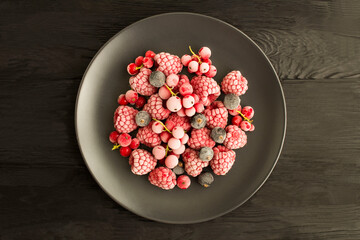 Frozen berries  in the black plate in the center of  the black wooden background. Top view. Copy space.