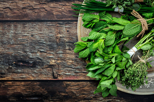Top view of round plate filled with various fresh green aromatic herbs placed on wooden table