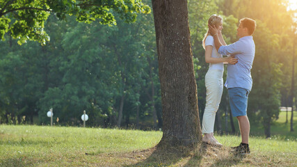 Fototapeta premium A young man and woman are standing under a tree in a park and hugging.