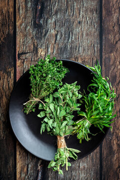 Top view of round plate filled with various fresh green aromatic herbs placed on wooden table
