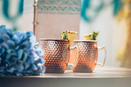 Cold Moscow Mule cocktail with ginger beer and vodka with lime served in traditional copper mugs on bar counter with flowers