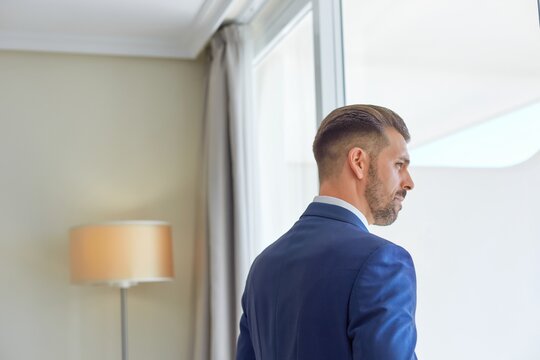 Smiling fiance in classy suit standing in bright living room of modern apartment during wedding fees