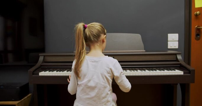 Little girl playing piano at home. Kid play piano in living room. Child learning piano at home. Music lesson, medium shot rear view.