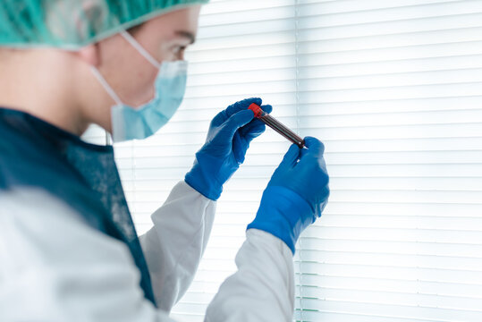 Side view of focused medical specialist in protective mask and latex gloves checking test tube with blood sample of patient while working in laboratory