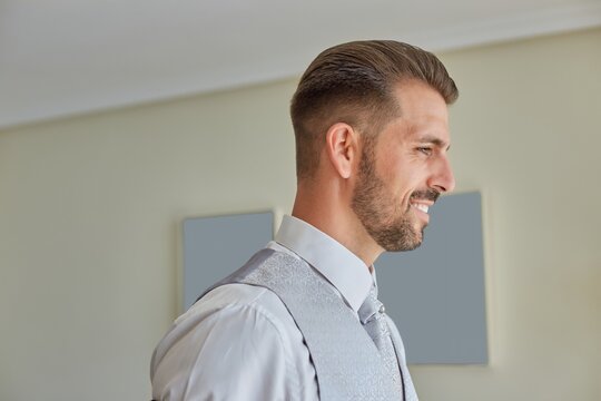 Smiling fiance in classy suit standing in bright living room of modern apartment during wedding fees
